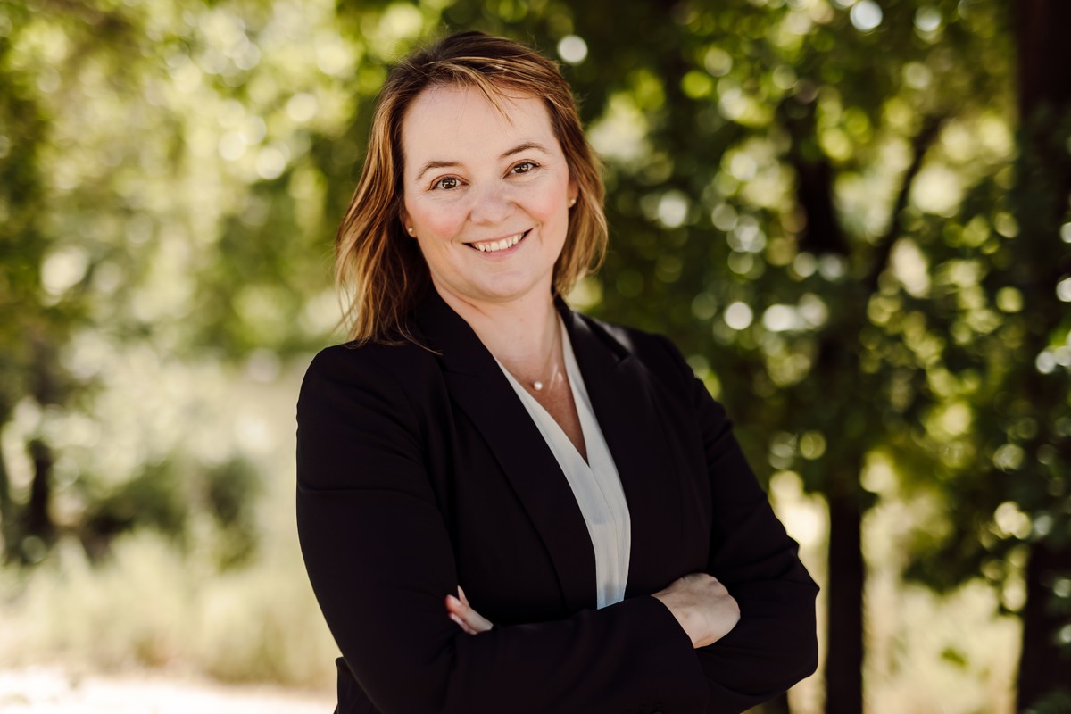 Client in a black blazer and white blouse, arms crossed, outdoors among green trees