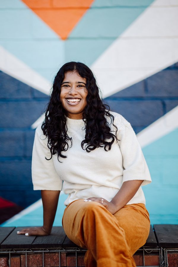 Headshot client in a cream sweater, seated in front of a blue and orange painted mural