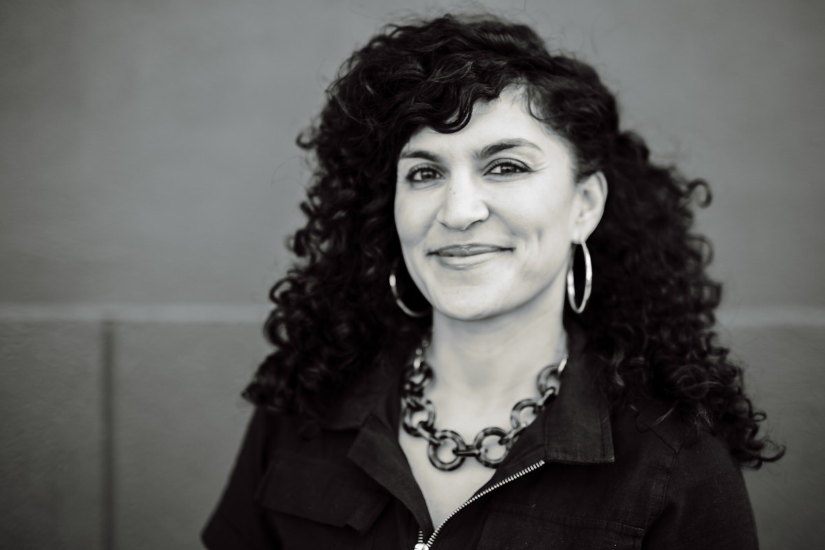 Black and white headshot of a client with long dark curls, hoop earrings and a chain necklace